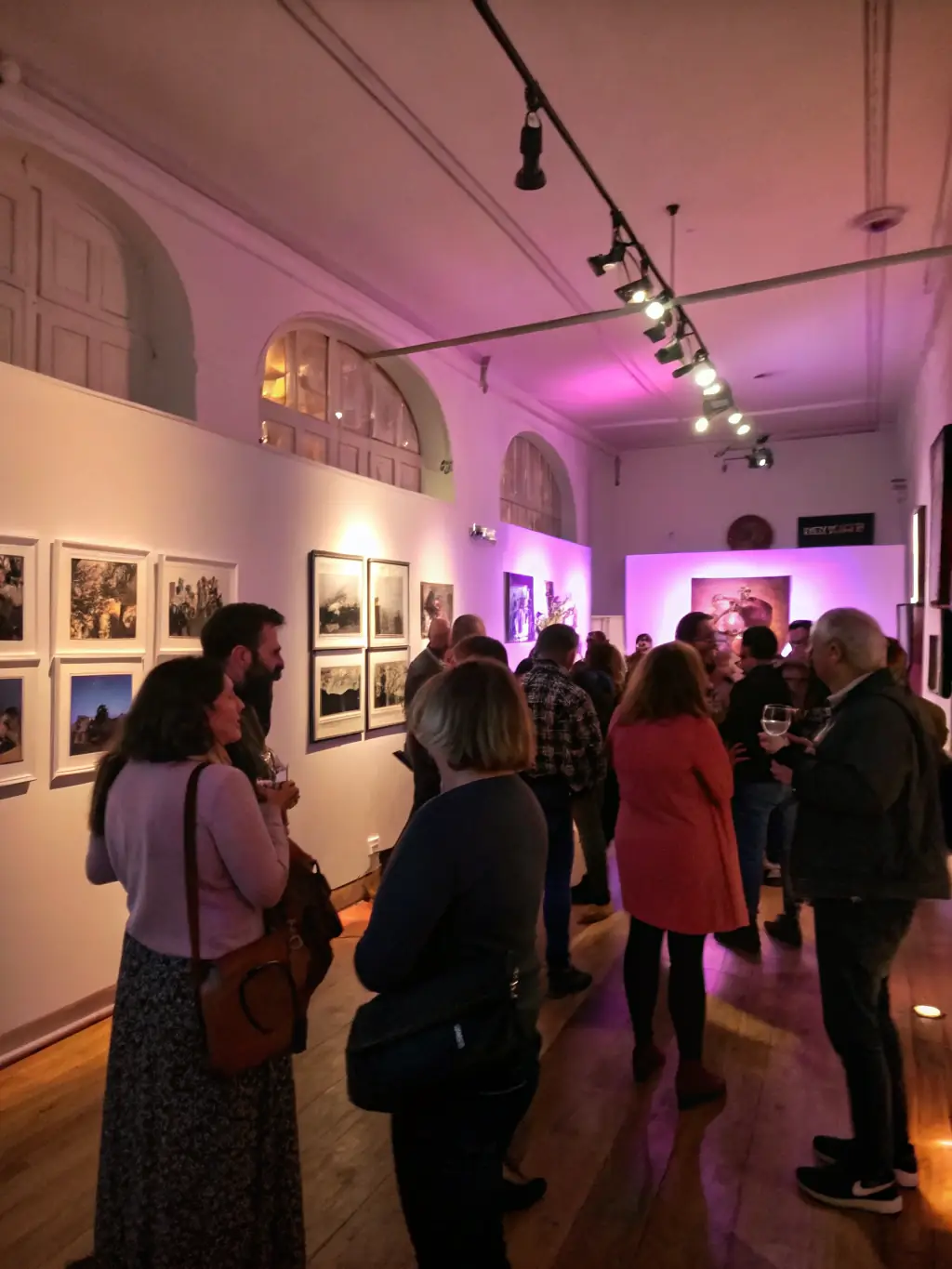 A photograph of an art exhibition opening night, with people mingling and admiring the artwork, showcasing a vibrant and engaging atmosphere.
